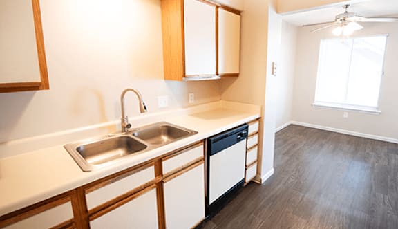 A kitchen with a sink, dishwasher and wooden cabinets.