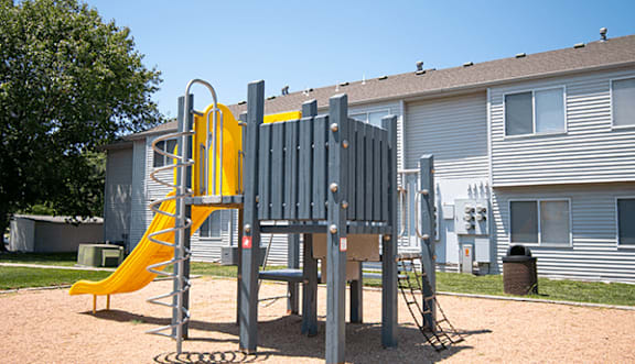 A playground with a yellow slide and a grey play structure.