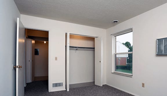 A room with a grey carpet and a window showing a view of a house.