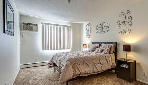 A bedroom with a bed, nightstand, and window with blinds.
