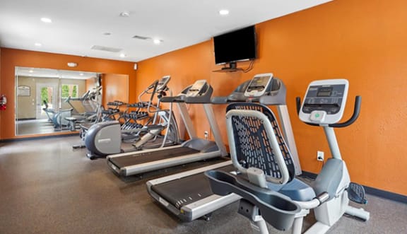 a gym with cardio equipment and a tv on the wall