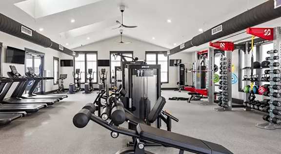 A gym with a variety of equipment including treadmills, weights, and a fan. at The Lofts at Town Madison, Madison, AL