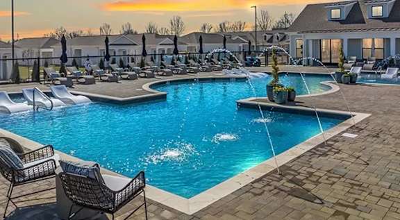 A swimming pool surrounded by lounge chairs and umbrellas at sunset. at The Lofts at Town Madison, Madison, AL