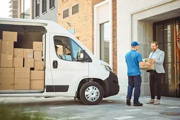 A white van is parked on the street with a man in a blue shirt and a man in a grey shirt standing next to it.