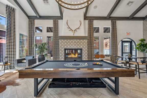 A pool table is in the middle of a room with a fireplace and a deer head mounted on the wall.