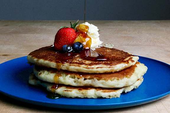 A stack of pancakes topped with whipped cream, strawberries, blueberries, and syrup.