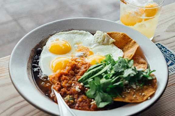 A bowl of food with eggs and a glass of juice.
