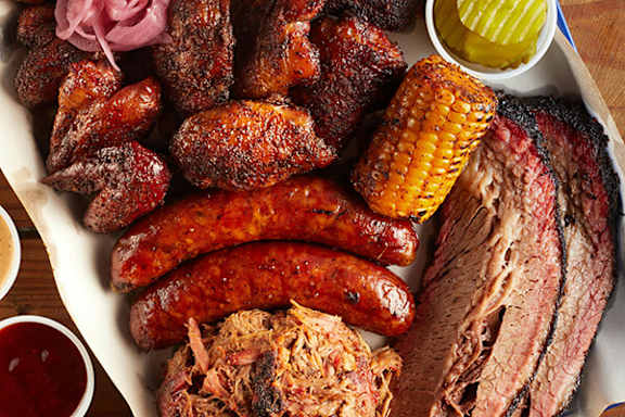 A platter of various meats including sausages, ribs, and pulled pork.