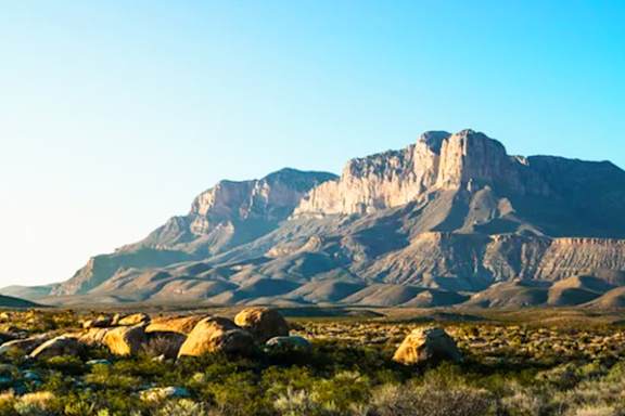 A large mountain with a flat top rises over a rocky landscape.