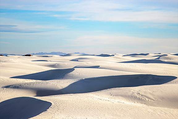 A vast desert landscape with rolling sand dunes under a clear blue sky.