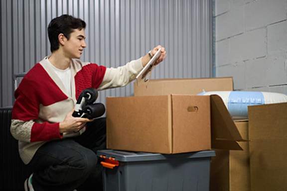 A man is packing a box with a tape dispenser.