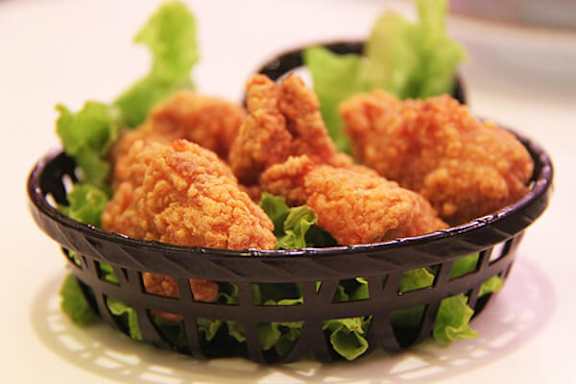 Fried chicken pieces in a black basket on a white plate.