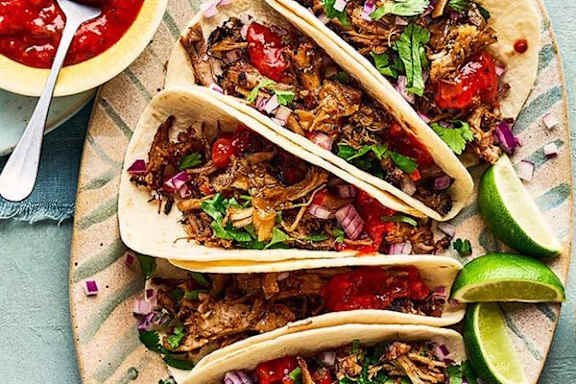 Three tacos with meat, onions, and cilantro on a plate.