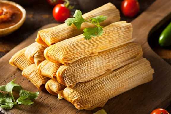 A pile of freshly made tamales on a wooden board.
