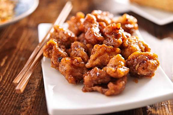 A plate of glazed chicken with chopsticks on a wooden table.