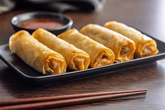 A plate of fried spring rolls with a side of dipping sauce.
