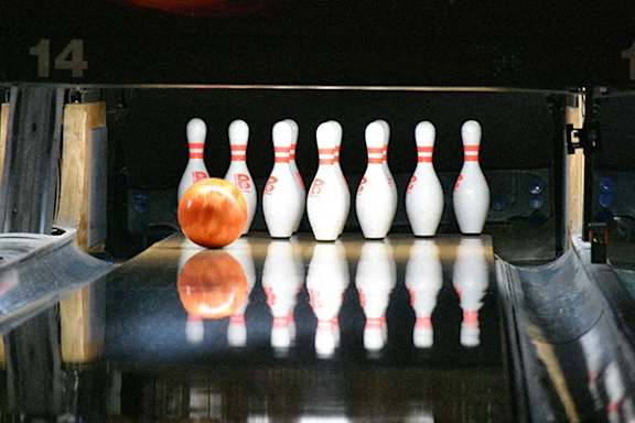 A bowling ball is about to hit the first pin in a game of bowling.