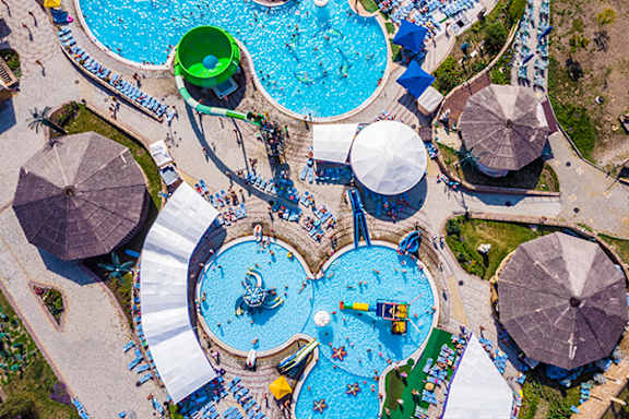 An aerial view of a water park with a large blue pool and a smaller green pool.