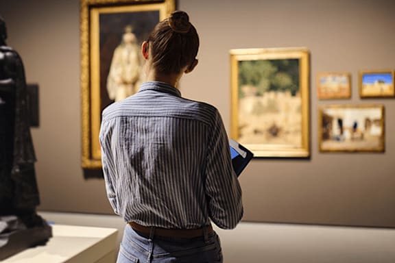 A woman in a striped shirt is looking at paintings in a gallery.