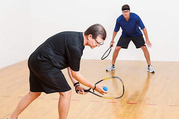 Two men playing tennis on a wooden court.