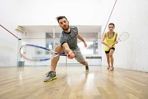 A man and a woman playing squash in a squash court.