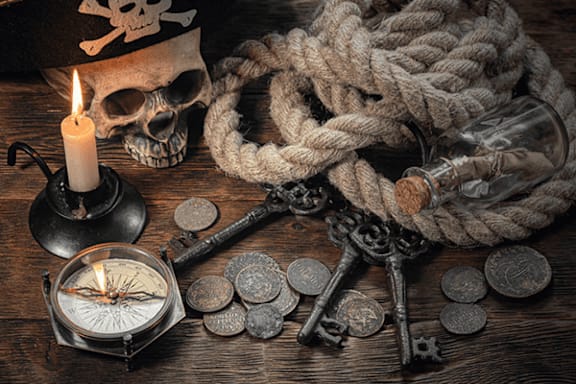 A skull, a candle, a rope, a compass, and old keys are arranged on a wooden surface.
