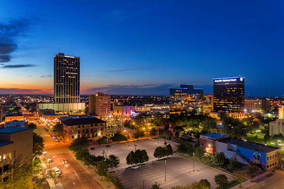 A cityscape at dusk with a large parking lot in the foreground.