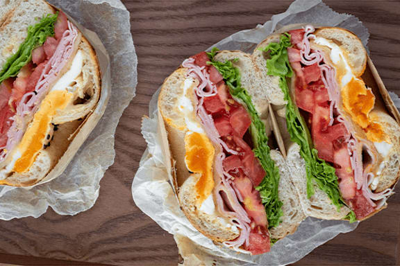 Two sandwiches with lettuce, tomato, and ham on white bread.
