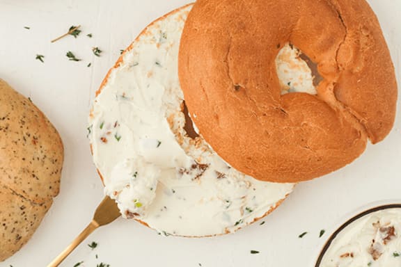 A bagel with cream cheese and herbs on top.