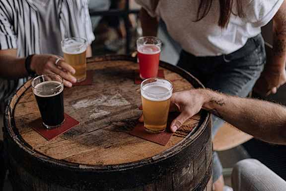 Four people are sitting around a wooden barrel with glasses of beer.