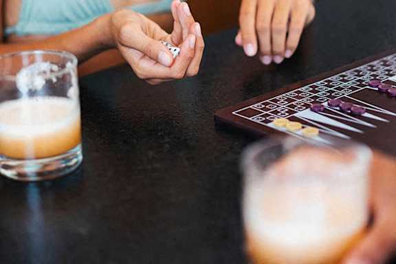 A person is playing a board game with beer glasses on the table.