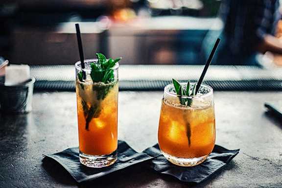 Two glasses of a fruity beverage with mint leaves and ice cubes.