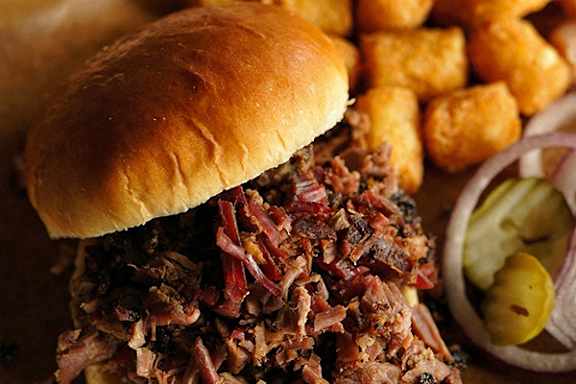 A close up of a pulled pork sandwich with pickles and fries.