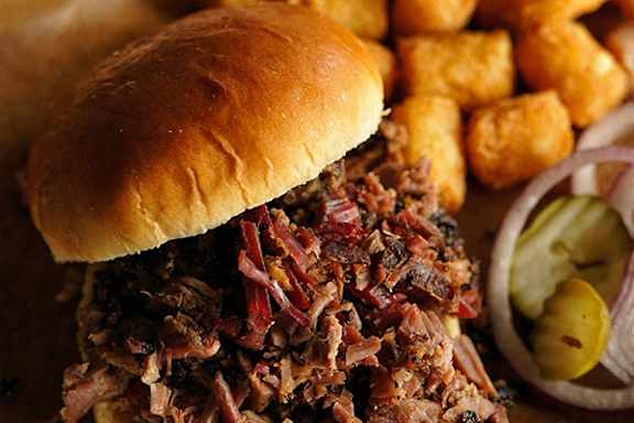 A close up of a pulled pork sandwich with pickles and fries.