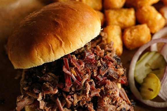 A close up of a pulled pork sandwich with pickles and fries.