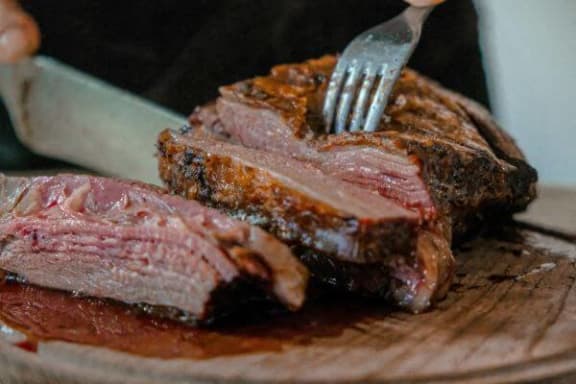 a fork cutting into a piece of steak on a cutting board