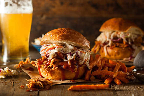 Two pulled pork sandwiches with coleslaw and fries on a wooden table.