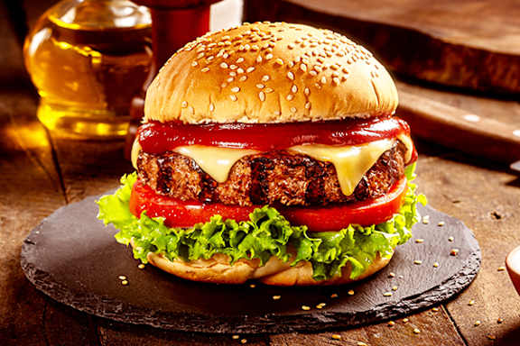 A burger with cheese, tomato, and lettuce on a sesame seed bun.