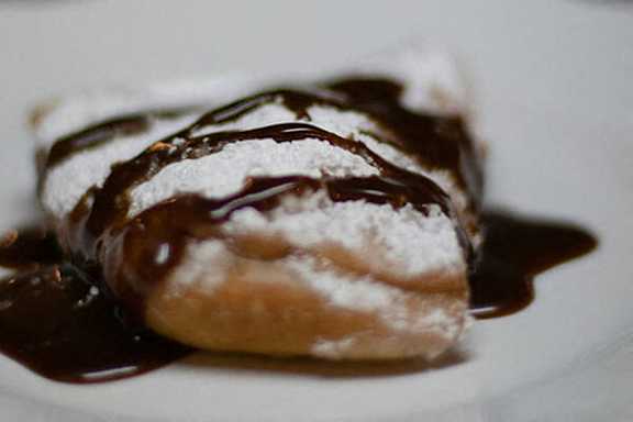 A chocolate covered pastry with powdered sugar on top.