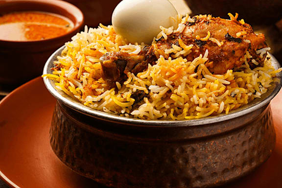 A dish of biryani with a boiled egg and a side of sauce.