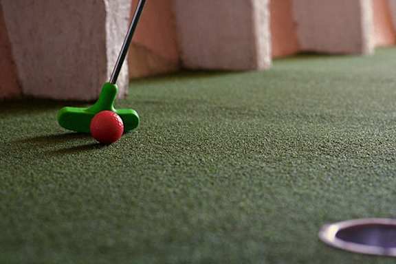 A golf ball is on the green with a hole in the background.