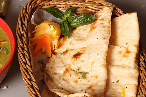 A basket contains a folded flatbread and a bowl of green sauce.