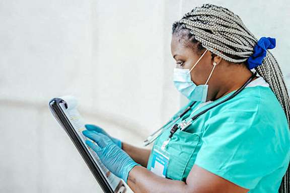 A woman in a teal scrub top and blue gloves is using a tablet.