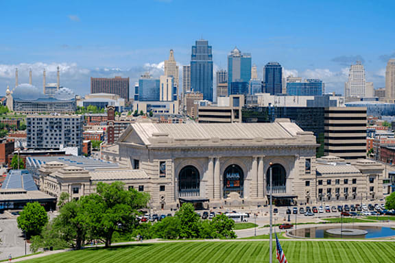 A large building with a flag on it is in the foreground of a city skyline.
