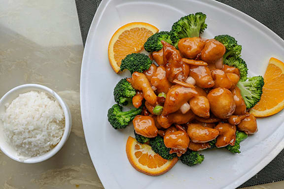 A plate of food with broccoli, orange slices, and a bowl of rice.