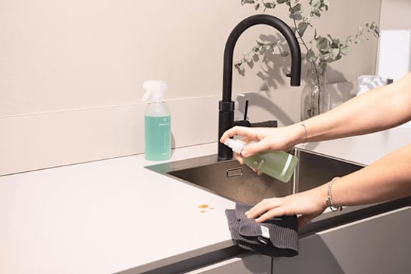 A person is cleaning a sink with a spray bottle and a cloth.