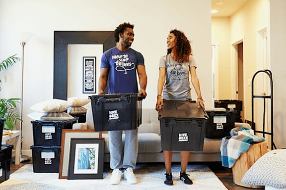 A man and woman are standing in a living room surrounded by moving boxes.