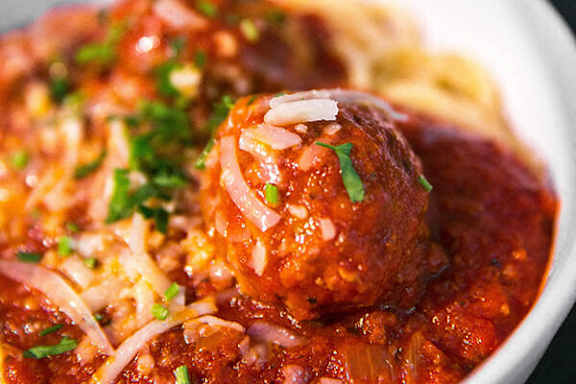A close up of a meatball in a red sauce with grated cheese on top.