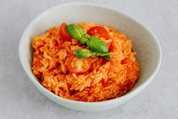 A bowl of orange rice garnished with basil leaves and tomato slices.