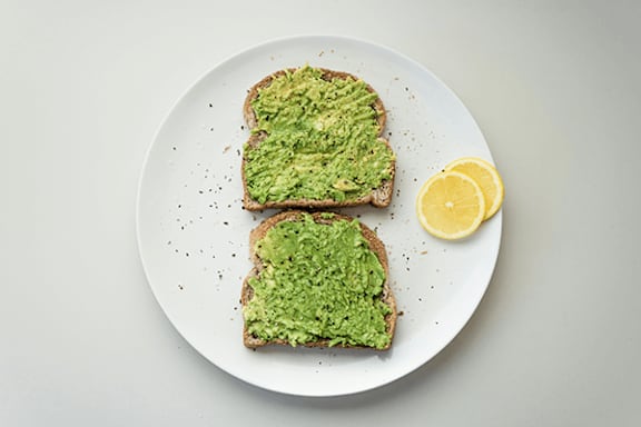 Two slices of toast with green spread and a wedge of lemon on a white plate.
